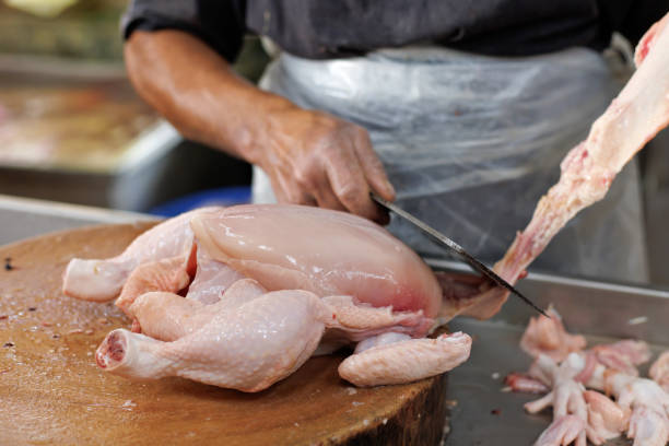 Cropped image of an Asian butcher chopping raw chicken meat at market stall
