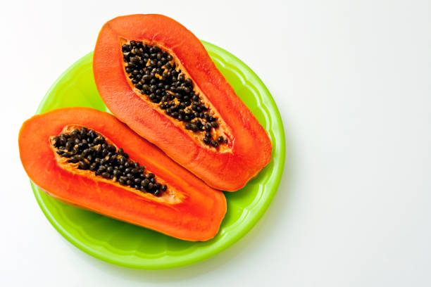 fresh papaya halves with seeds on a green plate, white background